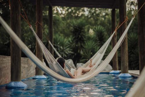 a woman sitting in a hammock next to a swimming pool at La Posada en el Potrero Chico in Hidalgo