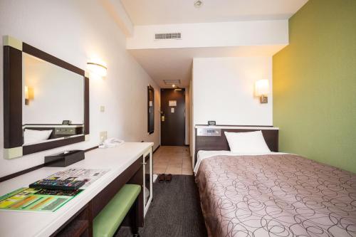 沼津市にある三交イン沼津駅前のベッドと鏡が備わる小さなホテルルームです。