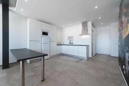 a white kitchen with a table and a refrigerator at Durmiendo sobre el mar, El Echadero in Telde