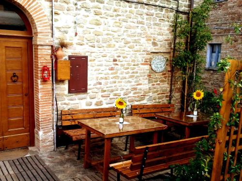 un patio con 2 mesas y bancos junto a una pared de ladrillo en Al Castello di Montalfoglio en San Lorenzo in Campo
