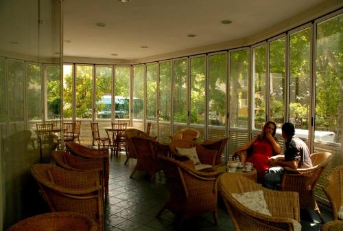Dos personas sentadas en mesas en un restaurante con ventanas en Hotel Arno en Rímini