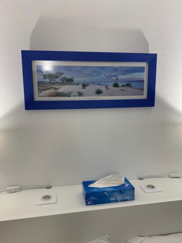 a picture of the beach in a blue frame on a shelf at Le Melchior in Sainte-Terre