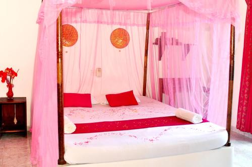 - une chambre avec un lit à baldaquin rose et des oreillers rouges dans l'établissement Surewo Sun Shine Apartment, à Bentota