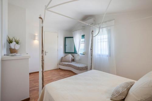 a white bedroom with a bed and a chair at Acroyali Beach House in Pefkohori