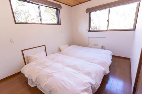 a bedroom with two white beds and two windows at Guest house Japan Kita-Karuizawa in Saikubo