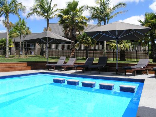 a swimming pool with chairs and umbrellas next to at Kerikeri Homestead Motel & Apartments in Kerikeri