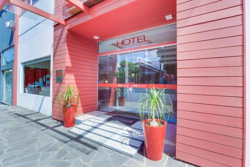 a red building with two potted plants in front of a hotel at Hotel Comoditá Ltda in Sapiranga