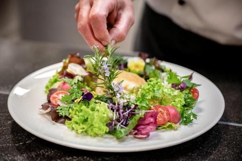 a person preparing a salad on a white plate at Insel Hotel Bonn - Superior in Bonn