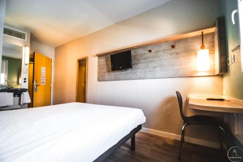 1 dormitorio con cama, escritorio y TV en la pared en ibis budget Saint-Brieuc Yffiniac, en Yffiniac