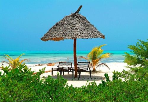 two benches under an umbrella on a beach at Hakuna Majiwe Beach Lodge in Paje