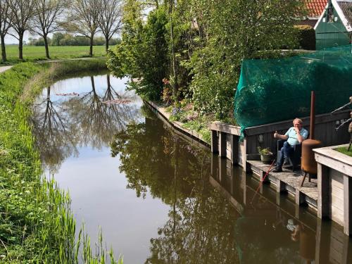 a woman sitting on a dock next to a river at B&B De Gulden Halsband Pingjum in Pingjum