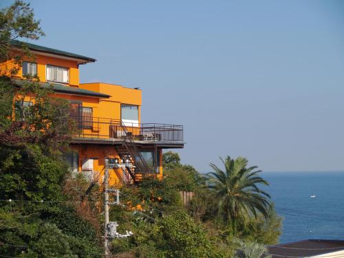 伊東的住宿－休閒海灘公社（僅限成人），一座黄色的房子,在山边,与大海