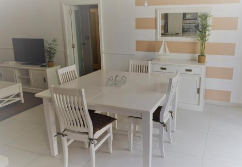 uma sala de jantar branca com uma mesa e cadeiras brancas em Orchid Court Apartment. em Għajnsielem