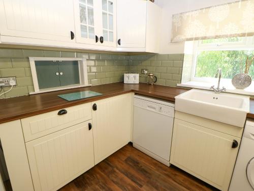 a kitchen with white cabinets and a sink and a window at Bilberry Nook Cottage in Westgate