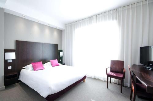a bedroom with a bed with pink pillows and a desk at Best Western Plus Hotel Plaisance in Villefranche-sur-Saône