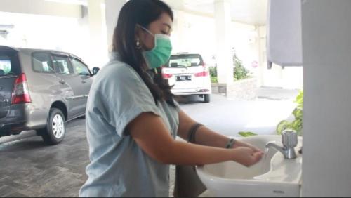 a woman in a mask washing her hands in a sink at Swiss-Belinn Tunjungan Surabaya in Surabaya