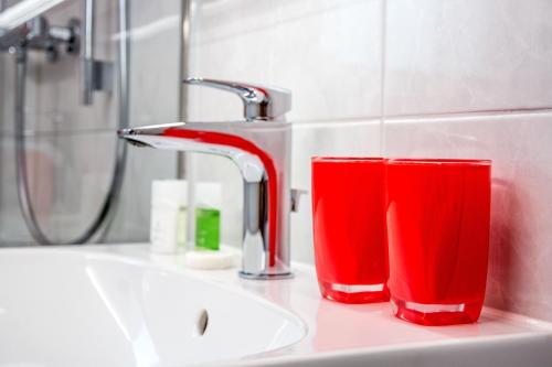 deux verres rouges assis sur un évier à côté d'un robinet dans l'établissement Apartment Dolomit DG - GRIWA RENT AG, à Grindelwald