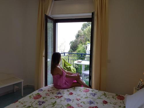 a woman sitting on a bed in front of a window at Hotel Oriente in Vico Equense