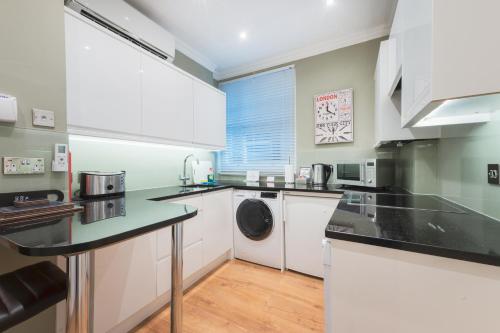 a kitchen with white cabinets and a washer and dryer at No1 The Mansions By Mansley in London