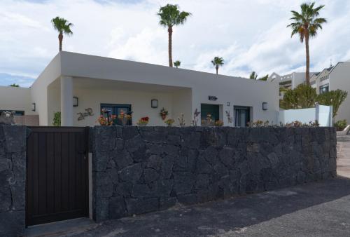 a white house with palm trees behind a stone wall at luxury casa playa roca bord de mer in Costa Teguise