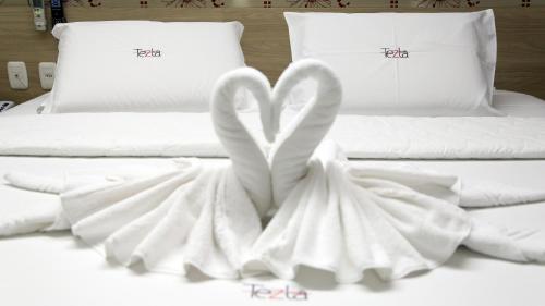 two white beds with towels in the shape of hearts at Tezla Hotel in Primavera do Leste