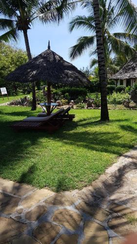 a picnic table with a straw umbrella on the grass at Crystal Bay Resort in Watamu