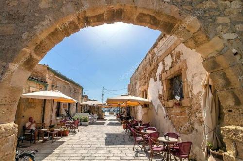 an archway with tables and chairs and umbrellas on a street at Colle Alto Pachino - Marzamemi in Pachino