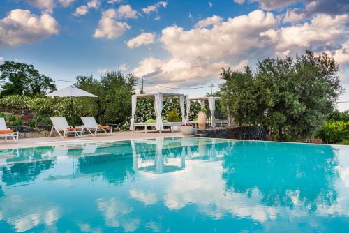 a swimming pool with blue water and two chairs and an umbrella at Kepos Etna Relais & Exclusive Spa in Santa Venerina