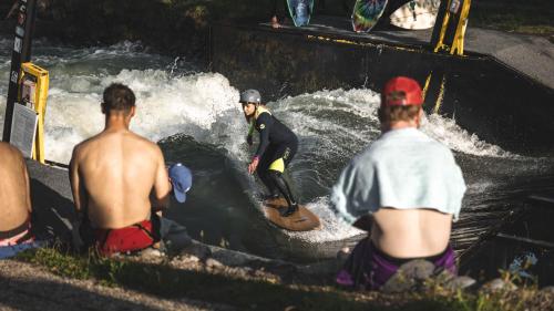 a group of people watching a man on a surfboard in a river at Hotel and Park Divoká Voda in Bratislava
