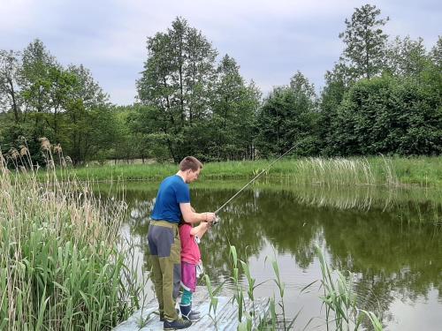 a man and a child fishing in a pond at Domek Drewniany in Nowa Wola