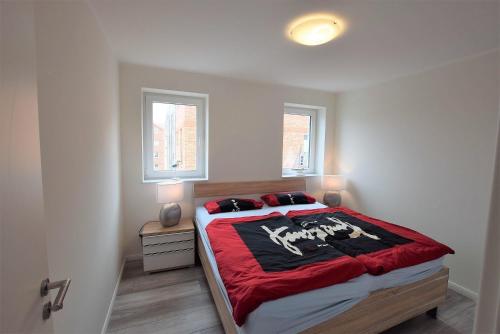 1 Schlafzimmer mit einem Bett mit einer roten Decke und 2 Fenstern in der Unterkunft Meeresblick "Jakobsmuschel" Haus 1, WE 8 in Hohwacht
