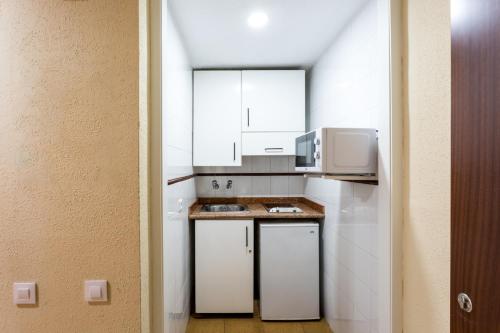 una pequeña cocina con armarios blancos y microondas en Apartamentos Resitur, en Sevilla