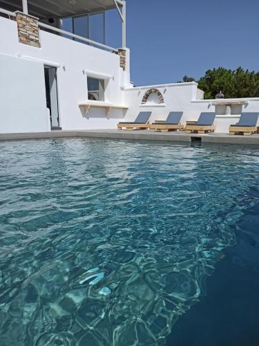 a swimming pool with blue water in front of a house at Porto Raphael Residences & Suites in Agios Ioannis Tinos