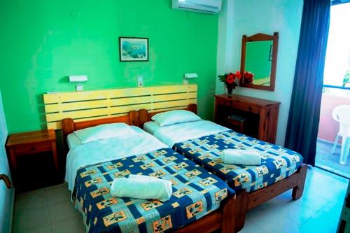 two beds in a bedroom with green walls and a mirror at Marika Apartments in Mastichari