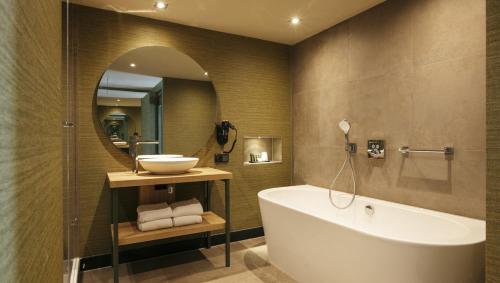 a bathroom with a tub and a sink and a mirror at Van der Valk Hotel Apeldoorn - de Cantharel in Apeldoorn