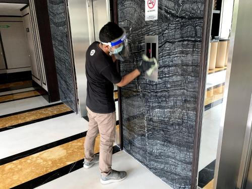 a man wearing a face mask and gloves putting a ticket into an elevator at The Alts Hotel in Palembang