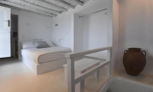 a white bedroom with a bed and a vase at The stone in Tinos