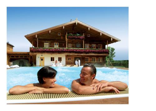 a man and woman laying in a swimming pool with a house at Fichtenwald-Ihr Boutique I Glück`s Hotel in Bad Füssing