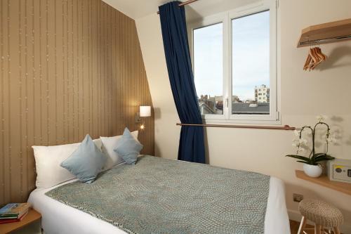 Un dormitorio con una cama con almohadas azules y una ventana en Hôtel Villa Sorel - Paris Boulogne, en Boulogne-Billancourt