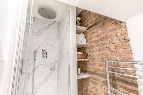 a bathroom with a walk in shower next to a brick wall at Charming cottage in WINDSOR - WALK TO CASTLE &SHOPS! in Windsor