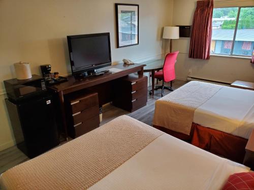 a hotel room with two beds and a desk with a television at Alpine Inn Abbotsford in Abbotsford