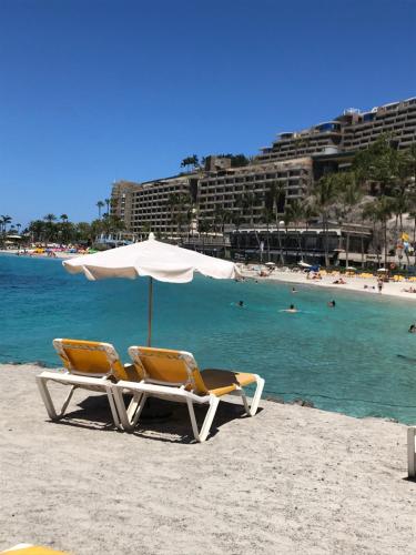 two lounge chairs and an umbrella on a beach at Anfi del Mar in La Playa de Arguineguín