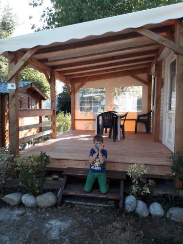 un jeune garçon assis sur une table de pique-nique sur une terrasse couverte en bois dans l'établissement mobil home, à Médis