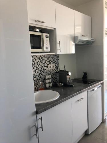 une cuisine blanche avec un évier et un micro-ondes dans l'établissement Cap d'agde Naturiste Heliopolis AB Vue Mer, au Cap d'Agde