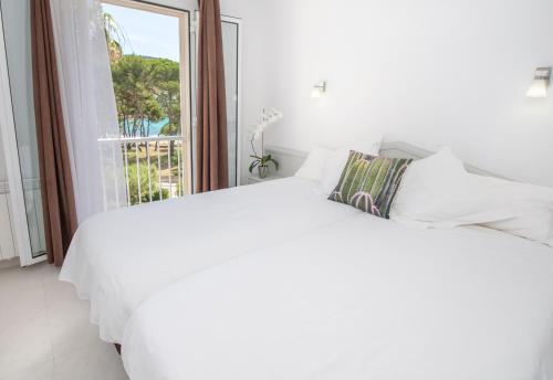 biała sypialnia z dużym białym łóżkiem i oknem w obiekcie Oros de Malasigeni Bl. III 3ºA w Canyamel