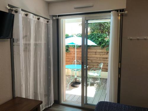 une porte coulissante en verre menant à une terrasse avec un parasol dans l'établissement Hotel de la Plage, à Gruissan