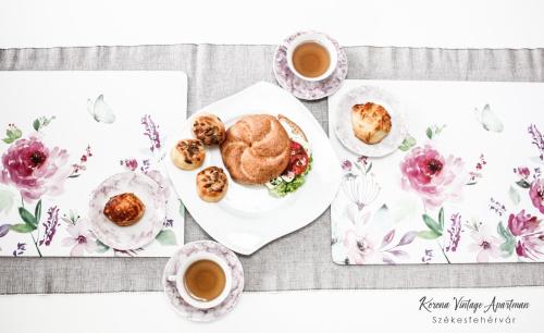 a table with a plate of food and two cups of coffee at Korona Apartman Székesfehérvár in Székesfehérvár