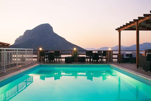 a swimming pool with a table and a mountain in the background at Kalymnos Village in Masouri