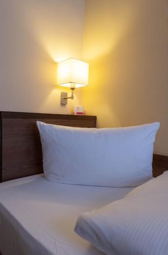 a bed with white pillows and a light on the wall at Hotel am Großen Waisenhaus in Potsdam