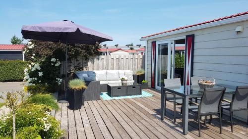 a wooden deck with a table and an umbrella at Olmenduin Chalet Olm Zeeland in Serooskerke